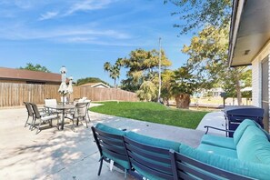 Eine Terrasse im Freien mit Esstisch und Stühlen, einer Couch und einem Rasen.
