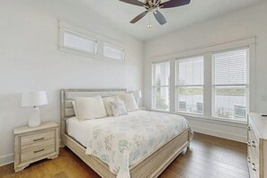 A bedroom with a bed, nightstands, a ceiling fan, and large windows. - Reserve Lane Retreat | Reserve at St Charles Bay (Rockport)