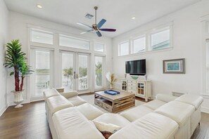 A spacious living room with a large sectional sofa, a coffee table, a television, and a ceiling fan. - Reserve Lane Retreat | Reserve at St Charles Bay (Rockport)