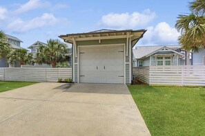 A garage with a covered entrance, a concrete driveway, and a white fence. - Reserve Lane Retreat | Reserve at St Charles Bay (Rockport)