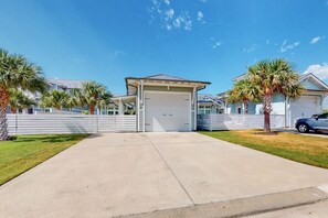 A residential property with a garage, a covered driveway, and a lawn with palm trees. - Reserve Lane Retreat | Reserve at St Charles Bay (Rockport)
