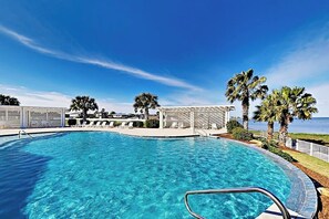 A clear blue pool with a poolside area, palm trees, and a view of the ocean. - Reserve Lane Retreat | Reserve at St Charles Bay (Rockport)