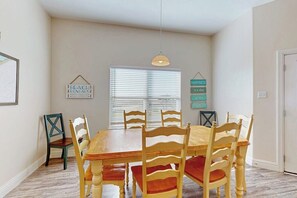 A dining area with a wooden table and chairs, a hanging pendant light, and a window with blinds. - Coral Reef Gataway - Pool, Playground & Bay Views (Rockport)
