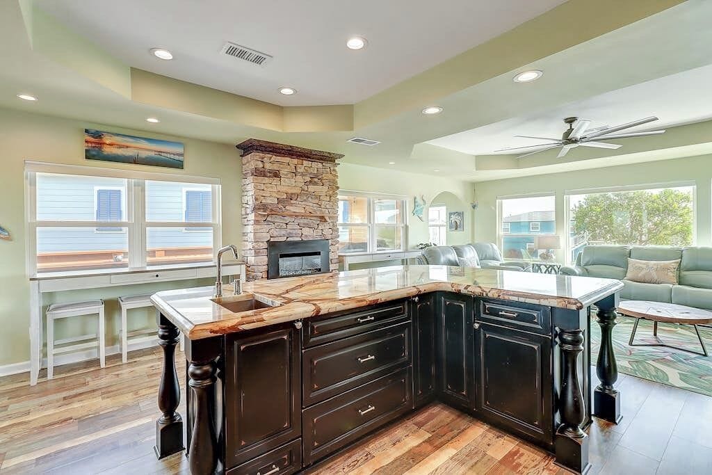 A spacious kitchen with a stone fireplace, dark cabinetry, and a large island.