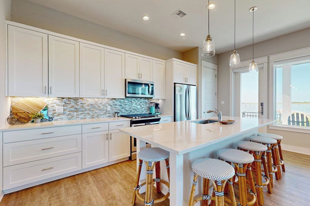A modern kitchen with white cabinets, a large island with bar stools, a microwave, and a refrigerator.