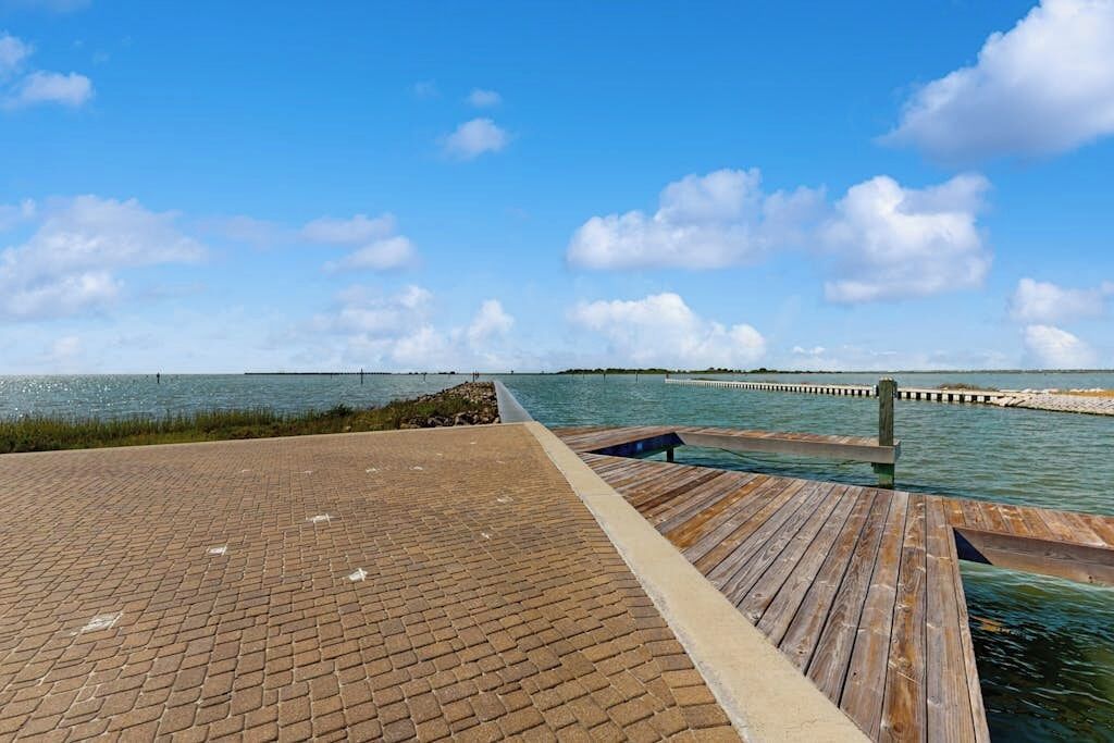 Une jetée en bois s’étendant sur une étendue d’eau calme, sous un ciel dégagé.