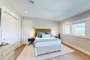 A bedroom with a bed, bedside tables, a dresser, and a window with a view. - Reserve at St Charles Bay Reserve Villa 601 (Rockport)