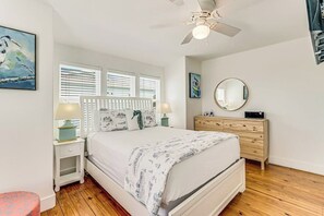 Une chambre à coucher comprenant un lit, des tables de chevet, une commode, un ventilateur de plafond et des œuvres d’art accrochées aux murs.