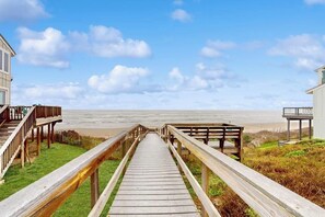 A wooden boardwalk leading to a beach with a clear sky and a distant view of the ocean. - Lost Colony Let The Sea Wash Away The Worries (Port Aransas)