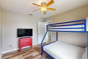 Ein Etagenbett mit Deckenventilator, ein Fernseher auf einer roten Kommode und eine weiße Tür.