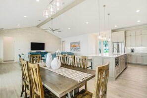 Une cuisine moderne avec des meubles blancs, un îlot central et un coin repas comprenant une table et des chaises en bois.