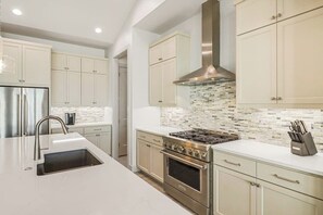 Een moderne keuken met roestvrijstalen apparatuur, een groot eiland met een spoelbak en lichtkleurige kastjes.