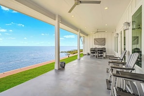 Un espace extérieur abrité, avec vue sur la mer, comprenant un coin salon avec des tables et des chaises.