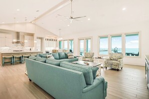 A spacious living area with a large teal sofa, a dining area with a kitchen in the background, and large windows offering a view of the ocean. - Casa Bahia San Carlos (Rockport)
