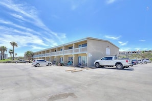A motel with a two-story structure, a parking lot, and a white pickup truck parked in front. - Ocean Wave - Pool, Walk to Beach & Town (Port Aransas)