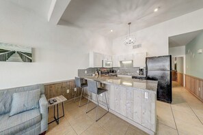 A modern kitchen with a central island, bar stools, and a dining area with a sofa. - Ocean Wave - Pool, Walk to Beach & Town (Port Aransas)