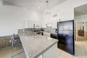 A modern kitchen with granite countertops, white cabinets, a black refrigerator, and a chandelier. - Ocean Wave - Pool, Walk to Beach & Town (Port Aransas)