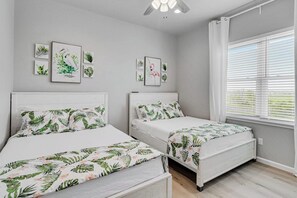 A bedroom with two beds, a ceiling fan, and artwork on the walls. - Dawn Patrol - Canal-Front, Dock & Pool (Rockport)