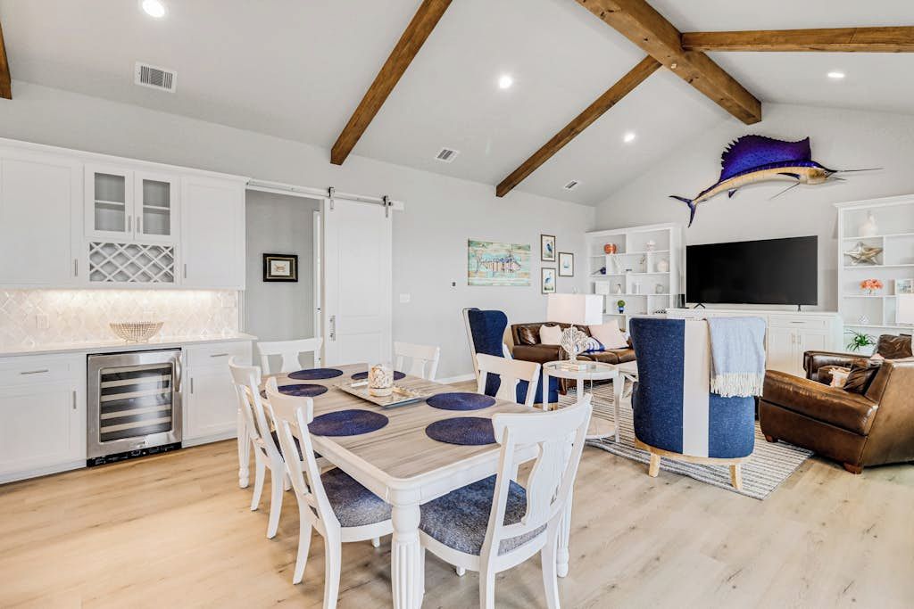 Una cocina moderna con armarios blancos, horno empotrado y comedor con mesa y sillas de madera.