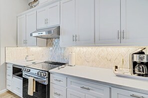 A kitchen with white cabinets, a stainless steel range hood, a built-in oven, and a coffee maker on the countertop. - Dawn Patrol - Canal-Front, Dock & Pool (Rockport)