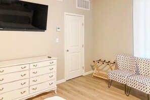 A room with a white dresser, a television mounted on the wall, a door, and a patterned sofa. - Dawn Patrol - Canal-Front, Dock & Pool (Rockport)