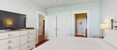 A hotel room with a bed, a television on a dresser, a ceiling fan, and a door leading to another room.