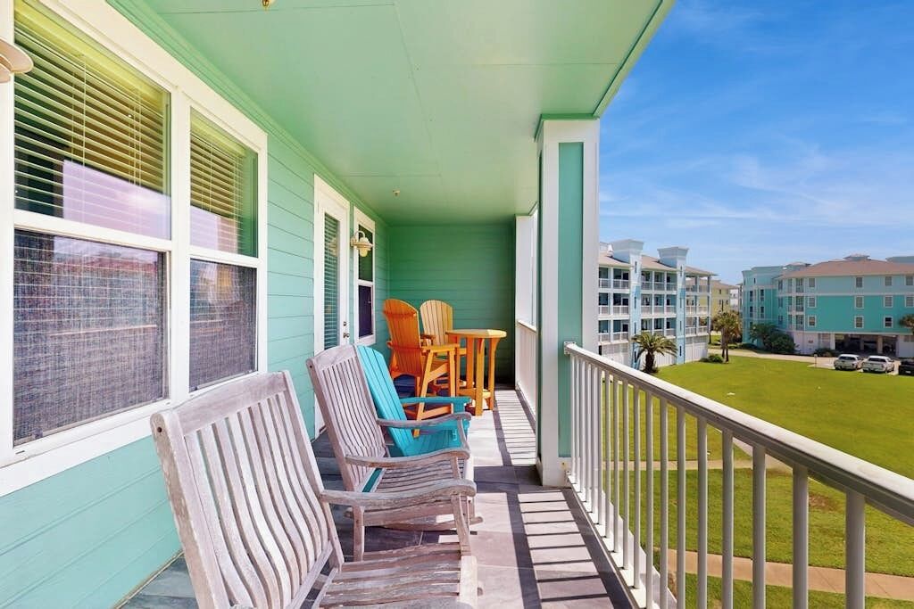 Une véranda avec des chaises et une table en bois, une balustrade de balcon et une vue sur un quartier résidentiel avec des immeubles.