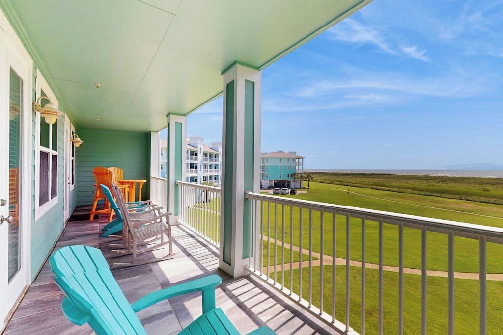 A balcony with chairs and a table, overlooking a grassy area and buildings.
