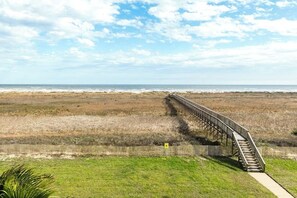 Un passeig marítim que condueix a la platja, amb una tanca de fusta i un cel serè.