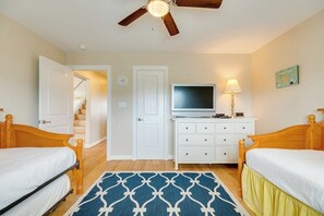 Ein Schlafzimmer mit zwei Einzelbetten, einem Deckenventilator, einem Fernseher, einer Kommode und einem gemusterten Teppich.