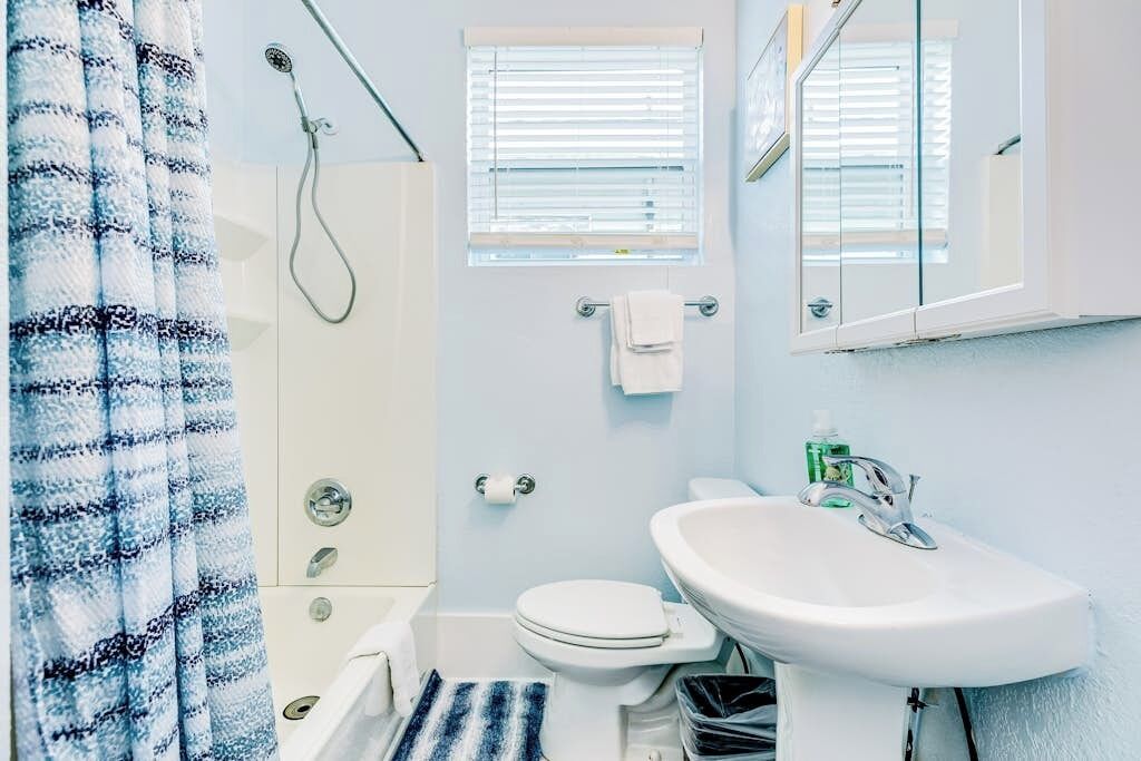 Ein Badezimmer mit Dusche, Toilette, Waschbecken und einem Fenster mit Jalousien.