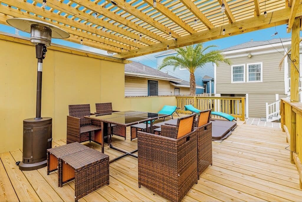 Um pátio externo com deck de madeira, móveis de vime, uma mesa e um aquecedor de pátio.