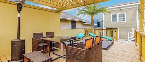 Eine Terrasse im Freien mit Holzdeck, Korbmöbeln, einem Tisch und einem Terrassenheizer.