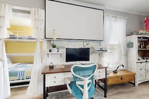 Un dormitorio con cama, escritorio con computadora, silla y televisor.