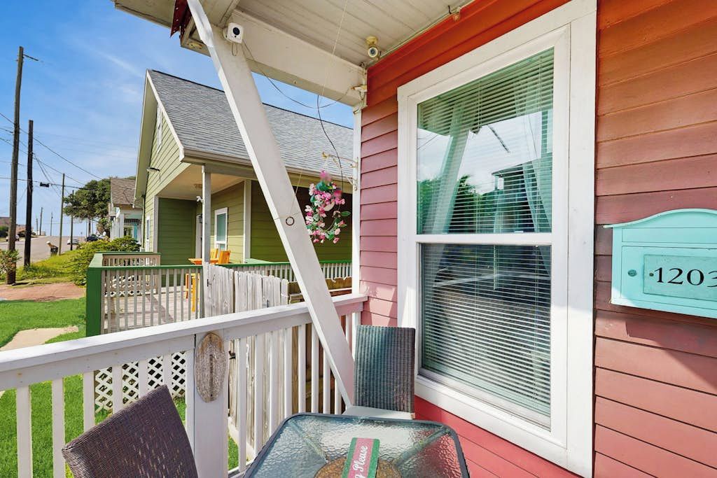 A porch with a chair, a window with a number plaque, and a white railing.