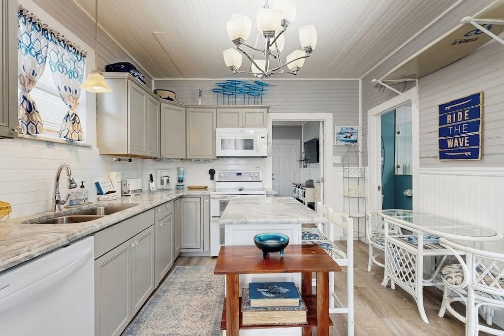 A kitchen with white cabinets, a central island, and a dining area with white chairs and a glass table.