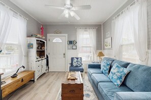 Una sala de estar con un sofá azul, una mesa de centro de madera, un armario blanco y un ventilador de techo.