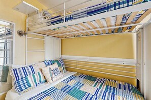 A bunk bed with a striped bedspread and pillows, a white headboard, and a window with a view. - Cowabungalow - Cozy Bungalow Near the Beach (Galveston)