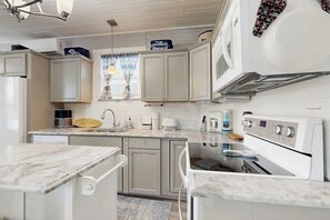 Una cocina con electrodomésticos blancos, encimera de mármol y ventana con cortinas.