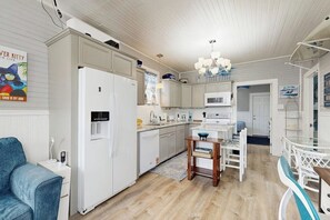 A modern kitchen with white cabinetry, a built-in microwave, and a dining area with a wooden table and chairs. - Cowabungalow - Cozy Bungalow Near the Beach (Galveston)