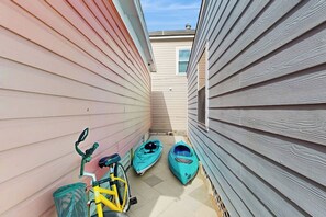 A narrow outdoor corridor with a bicycle and two kayaks parked against the walls. - Cowabungalow - Cozy Bungalow Near the Beach (Galveston)