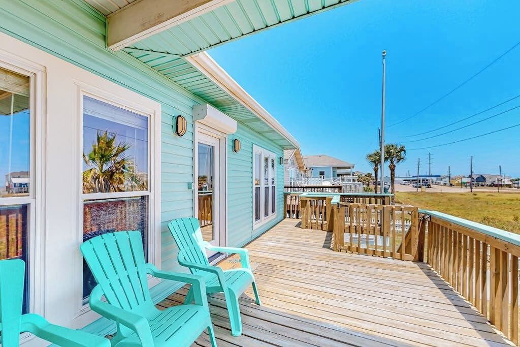 A wooden deck with two chairs, a railing, and a view of the beach.