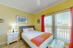 A bedroom with a bed, a nightstand, a window with blinds, and a wall with a picture. - Smiles in Isla Del Sol (Galveston)