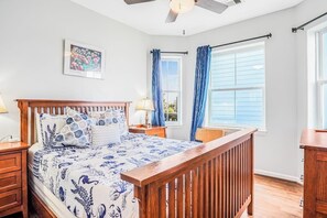 A bedroom with a wooden bed, a nightstand, a lamp, a window with curtains, and a ceiling fan. - 8-Mile Beachfront - Gulf Views & Dog-Friendly (Galveston)