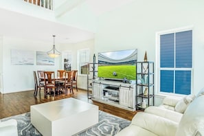 A spacious living room with a large flat-screen TV, a dining area with wooden chairs, and a white sofa. - 8-Mile Beachfront - Gulf Views & Dog-Friendly (Galveston)