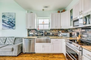 A modern kitchen with white cabinets, a stainless steel sink, a built-in oven, and a stone backsplash. - 8-Mile Beachfront - Gulf Views & Dog-Friendly (Galveston)