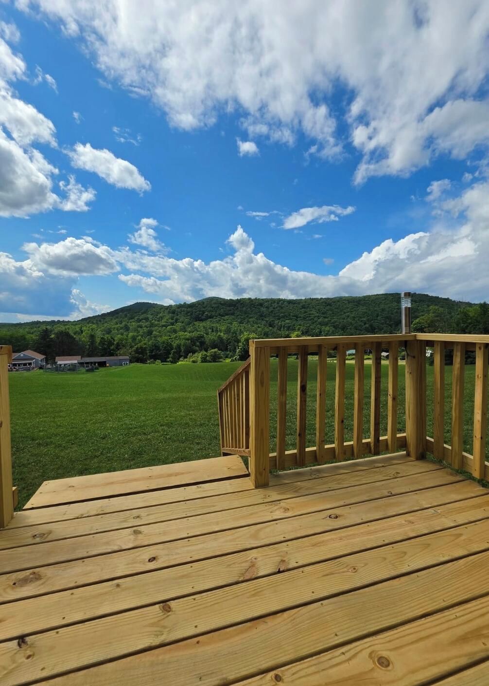A wooden deck with a view of a green field and a hill in the background.