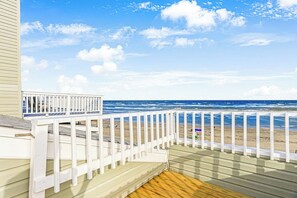 Eine Holzterrasse mit weißer Geländer, die auf einen Strand blickt.