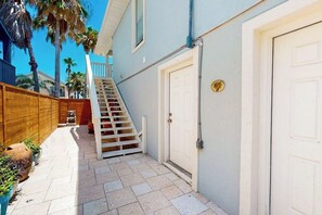 Ein Wohnhaus mit überdachter Terrasse, Holzzaun, weißer Tür und Treppe zu einem zweiten Stockwerk.