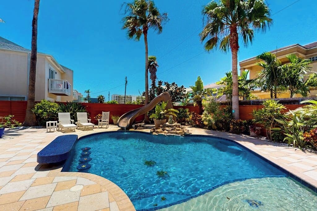 Una piscina con tobogán, rodeada de palmeras y sillas de descanso.